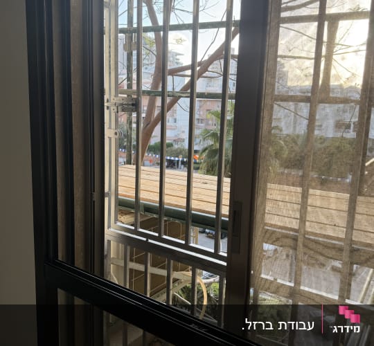 חלון עם סורגים ונוף חיצוני של בניינים ועצים